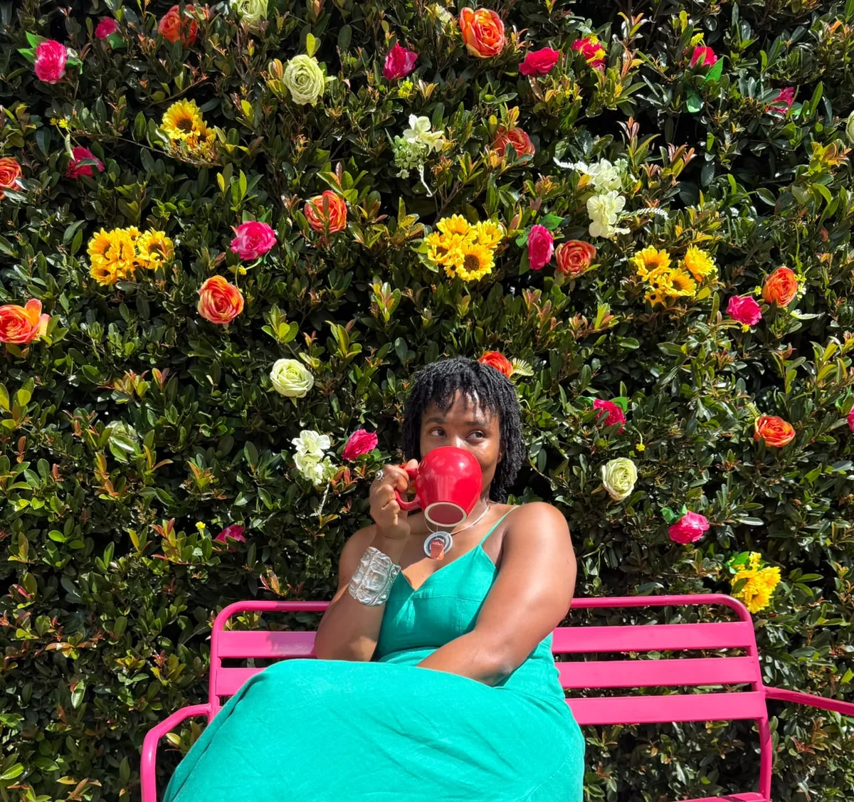 Tanya with a red mug in front of a colourful flower wall